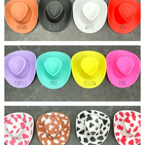 Puede incluir: Una colecci&oacute;n de sombreros de vaquero en miniatura en varios colores y patrones. Los sombreros incluyen colores lisos como marr&oacute;n, negro, blanco, rojo, morado, menta, amarillo y rosa. Tambi&eacute;n hay sombreros con dise&ntilde;os de estampado de vaca rosa, marr&oacute;n, negro y rojo. Cada sombrero tiene la etiqueta de su color o patr&oacute;n.