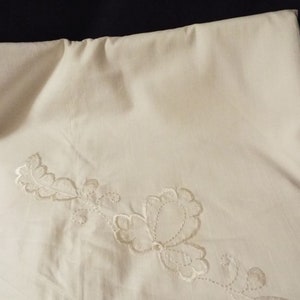 Op de afbeelding: Een wit linnen tafelkleed met een delicaat geborduurd bloemenmotief in crèmekleur.