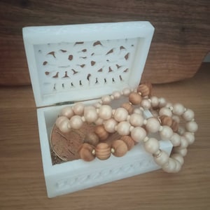 May include: White carved wooden box with a lid open, revealing a wooden and cream coloured beaded necklace inside.