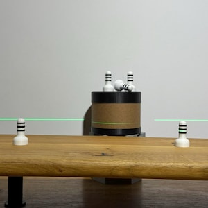 May include: A wooden table with three white and black striped objects. A cylindrical container with a brown paper wrap and black top holds more of the same objects. A green laser line is visible.
