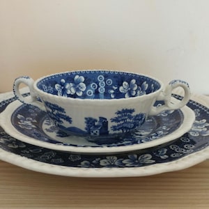 Może przedstawiać: Zestaw filiżanki i spodeczka z porcelany w kolorze niebieskim i białym z kwiatowym wzorem. Filiżanka ma dwa uchwyty, a spodeczek ma falisty brzeg.