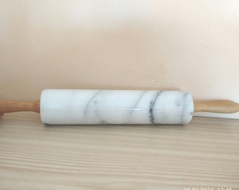May include: A white marble rolling pin with wooden handles. The marble has a gray veining pattern.