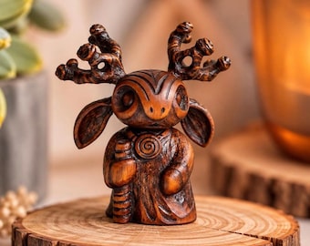 May include: A small, dark brown wooden figurine of a creature with large, branching antlers, prominent ears, and a spiral design on its chest. The figure stands upright, holding a staff-like object in one hand, with detailed carved textures.