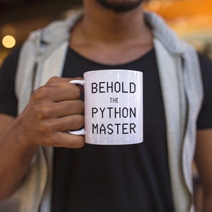 Puede incluir: Taza de cer&aacute;mica blanca con texto negro que dice "Behold the Python Master".