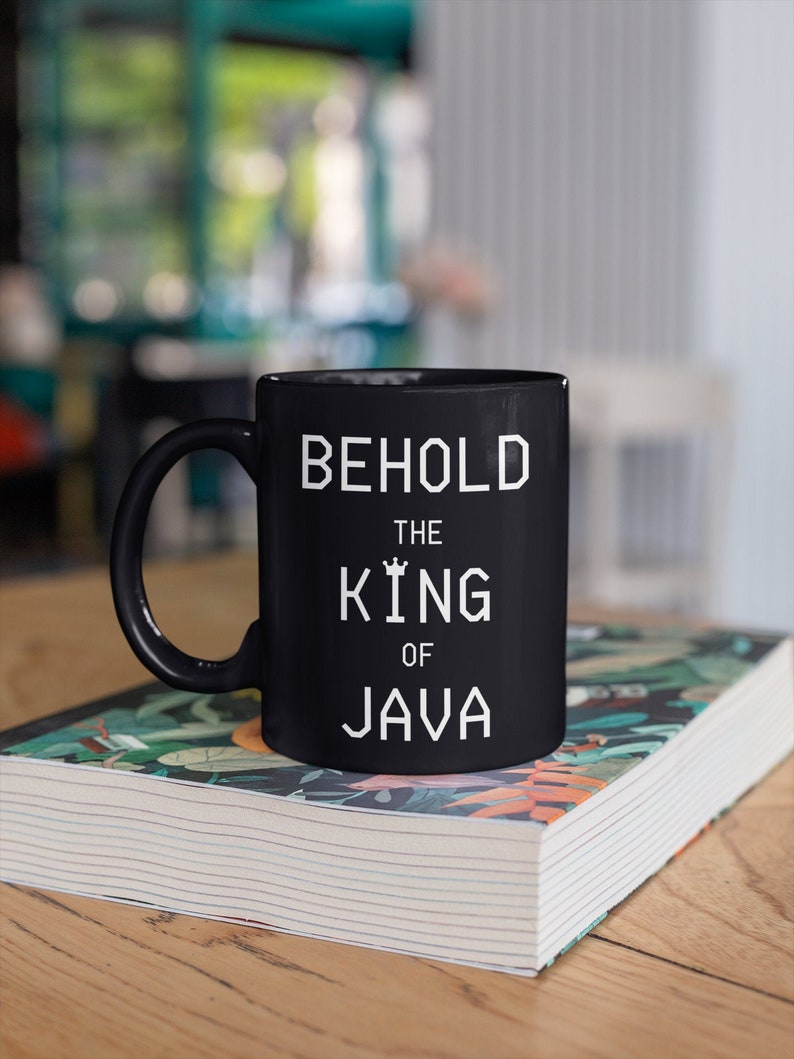 以下が含まれることがあります： 黒いセラミック製のマグカップで、白いデザインで「Behold the King of Java」と書かれています。
