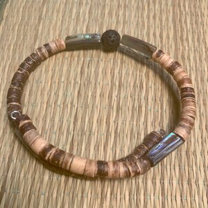 May include: A brown wooden bracelet with a silver metal accent and a black lava rock bead.