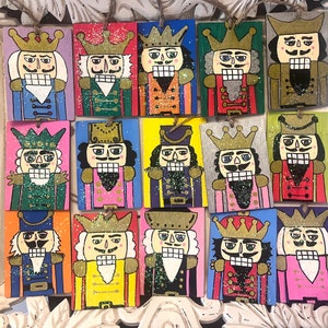 May include: Twelve wooden nutcracker ornaments, each with a different design. The nutcrackers are painted in bright colors, including red, blue, green, yellow, and pink. They have gold crowns and white beards.