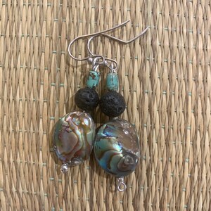 May include: A pair of earrings with silver hooks, turquoise beads, black lava rock beads, and iridescent abalone shell beads.