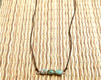 May include: A simple necklace with three turquoise-coloured beads on a brown cord.
