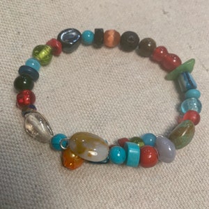 Puede incluir: Un brazalete de cuentas de colores con una variedad de piedras, incluyendo turquesa, rojo, verde y marrón.