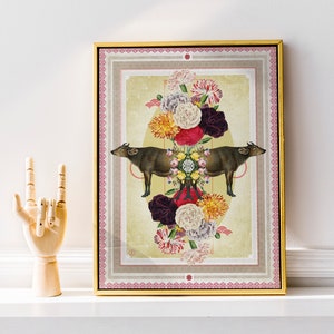 Op de afbeelding: Ingelijste kunstdruk met een symmetrisch ontwerp. Twee bruine waterbuffels kijken elkaar aan, omringd door een bloemstuk van rode, gele en witte bloemen. De lijst is goudkleurig.