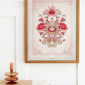 May include: A framed print with a pink background and a floral design featuring red flowers, green leaves, and two brown rabbits. The design is centered in the frame and has a gold and green border.