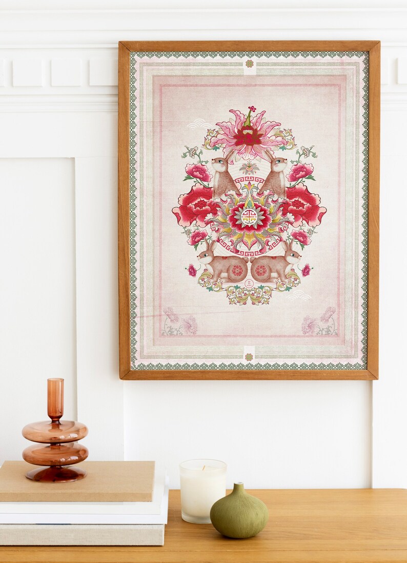 May include: A framed print with a pink background and a floral design featuring red flowers, green leaves, and two brown rabbits. The design is centered in the frame and has a gold and green border.