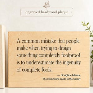 May include: A rectangular light-colored hardwood plaque featuring the engraved quote: A common mistake that people make when trying to design something completely foolproof is to underestimate the ingenuity of complete fools. — Douglas Adams, The Hitchhiker's Guide to the Galaxy.