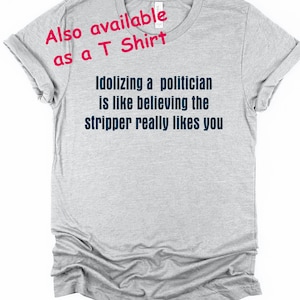 Pode incluir: T-shirt cinza claro com o texto "Idolizing a politician is like believing the stripper really likes you" em azul escuro. O texto "Also available as a T Shirt" &eacute; rosa.