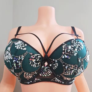 May include: A green bra with black straps and a decorative design. The bra features a sequined pattern in silver and iridescent colors. The straps have a unique crisscross design across the chest.