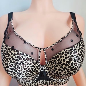May include: A leopard print bra with black accents and sheer mesh detailing. The bra features a keyhole design at the center and is displayed on a mannequin. The bra has adjustable straps and a classic silhouette.