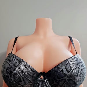 May include: A black and silver bra with a snakeskin pattern. The bra has adjustable black straps and a decorative clasp in the center. The bra is displayed on a mannequin.