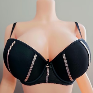 May include: Black bra with rhinestone accents. The bra features a classic design with underwire support and adjustable straps. Rhinestones are vertically aligned on the cups and center, adding a touch of sparkle. A small bow detail is centered between the cups.