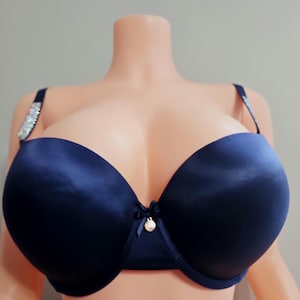 May include: A navy blue bra with a satin finish. The bra features a small bow and a pearl-like charm at the center. The straps are adorned with sparkling embellishments.