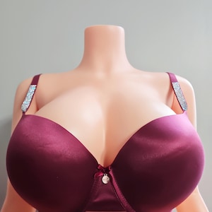 May include: A burgundy satin bra with rhinestone-studded straps. The bra has a bow and a small charm at the center. The bra is displayed on a mannequin.