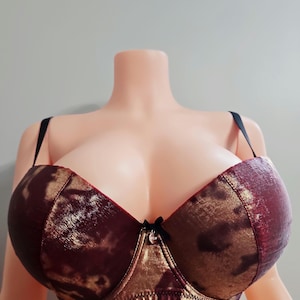 May include: A padded bra with a burgundy and gold animal print design. The bra has black straps and a small black bow in the center. The bra is displayed on a mannequin.