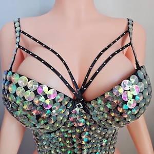 May include: A black bustier top adorned with iridescent, circular sequins. The top features a structured design with thin, black straps and a decorative embellishment at the center. The sequins create a shimmering effect, reflecting various colors.