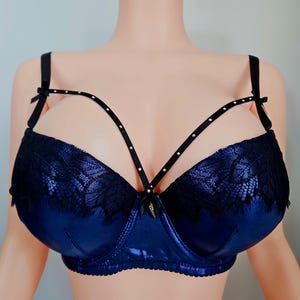 May include: A blue bra with black lace detailing and a strappy design. The bra features a shiny, satin-like material and small decorative bows. The straps are black and adorned with small, sparkling embellishments.