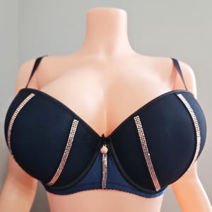 May include: A navy blue bra with rose gold rhinestone accents. The bra features a balconette style with adjustable straps and a small decorative detail at the center. The bra is displayed on a mannequin.