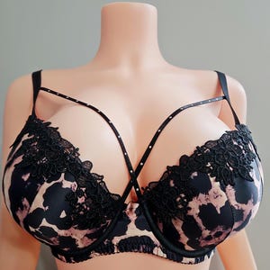 May include: A black and pink leopard print bra with black lace trim. The bra has a strappy design with small, decorative rhinestones. The bra is displayed on a mannequin.