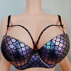May include: A mermaid-themed bra with a scale pattern in shades of purple and blue. The bra features black straps and a decorative harness with small silver studs. The cups are padded and have a shiny, iridescent finish.