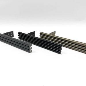 Puede incluir: Tres barras para cortinas en diferentes acabados: negro, gris oscuro y bronce. Cada barra tiene un soporte cuadrado y una serie de barras redondas y cil&iacute;ndricas.