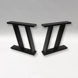 Può includere: Due gambe per tavolo in metallo nero dal design moderno. Ogni gamba ha una base rettangolare, due supporti angolati e una parte superiore rettangolare. Le gambe sono progettate per essere montate su un piano del tavolo.