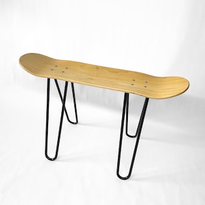 Könnte beinhalten: Eine Holzbank aus Skateboard mit schwarzen Metall-Haarnadelbeinen. Die Bank besteht aus einem einzigen Stück Holz und hat eine natürliche Holzoptik.