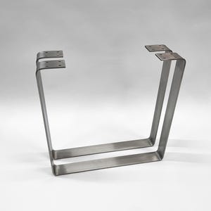 Könnte beinhalten: Zwei silberne Tischbeine aus Metall mit rechteckiger Form und einer leichten Biegung an der Oberseite. Die Beine sind aus robustem Metall gefertigt und haben eine gebürstete Oberfläche.