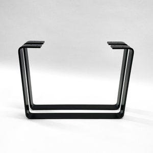 Könnte beinhalten: Zwei schwarze Metalltischbeine mit rechteckiger Form. Die Beine bestehen aus einem einzigen Stück Metall, das zu einer U-Form gebogen ist.