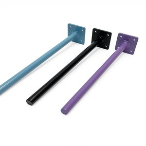 Op de afbeelding: Drie metalen plankdragers in verschillende kleuren: lichtblauw, zwart en paars. Elke drager heeft een vierkante metalen plaat aan de bovenkant en een ronde metalen staaf die naar beneden loopt.