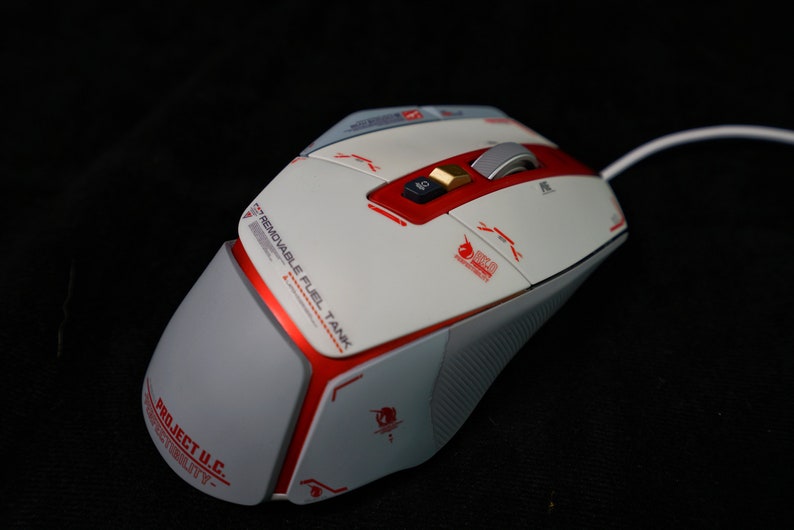 May include: A white and red gaming mouse with a removable fuel tank. The mouse has a gold button and a scroll wheel. The mouse is on a black surface.