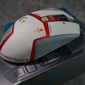 May include: A white and red wireless gaming mouse with a gold logo and a removable battery compartment. The mouse is on a gray box with the Logitech logo.