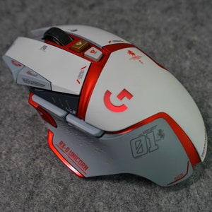 May include: A white and red gaming mouse with a red "G" logo and the text "RX-D UNICORN 01" on the side. The mouse has multiple buttons and a scroll wheel.