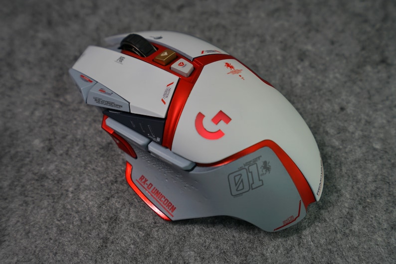 May include: A white and red gaming mouse with a red "G" logo and the text "RX-D UNICORN 01" on the side. The mouse has multiple buttons and a scroll wheel.