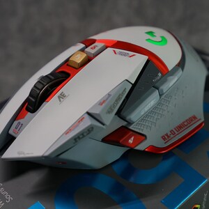 May include: A white and red wireless gaming mouse with a green light. The mouse has a scroll wheel, multiple buttons, and the text "RX-0 UNICORN" on the side.