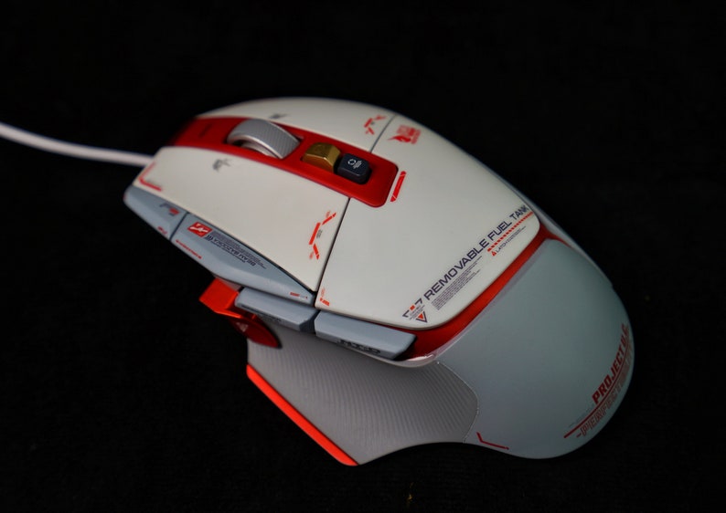 May include: A white and red gaming mouse with a textured gray side panel. The mouse has a red button labeled "F7 Removable Fuel Tank" and a gold button labeled "PROJECTIVE".