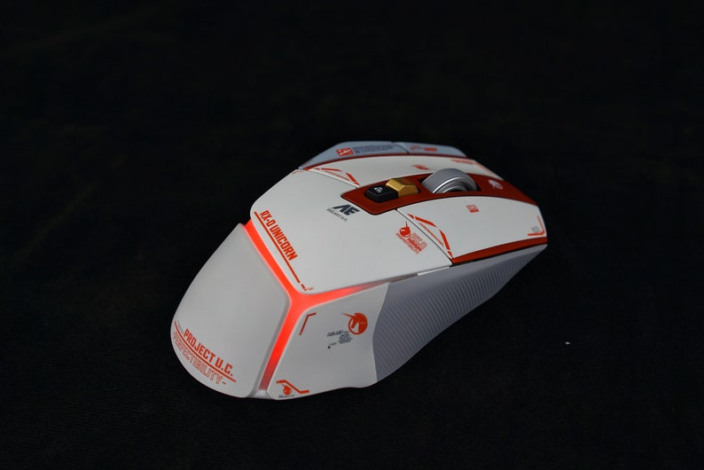 May include: A white and red gaming mouse with a red light on the side. The mouse has the text "Project U.C." and "RX-9 Unicorn" on it.