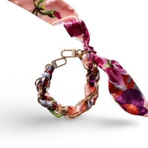 May include: A gold chain bracelet with a pink, purple, and green floral patterned fabric woven into the chain.
