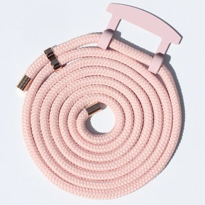 May include: A coiled pink phone strap with gold-colored metal accents. The strap is made of a thick, braided rope and features a pink plastic handle. The ends of the rope are capped with gold-colored metal.