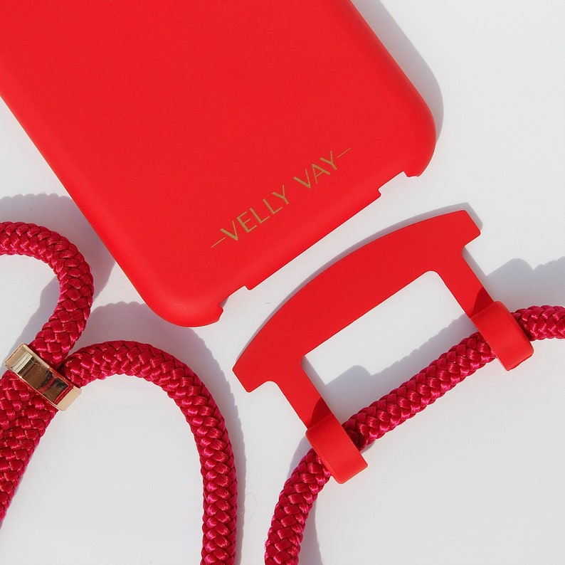 May include: A red phone case with a gold inscription that reads "Velly Vay" and a red phone strap with a gold accent.
