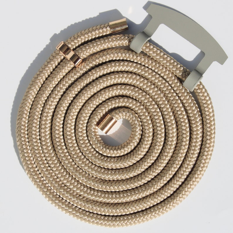 May include: A coiled beige rope with gold-colored metal accents and a gray handle. The rope is tightly woven, forming a spiral pattern. The handle is a light gray color and is attached to the rope.