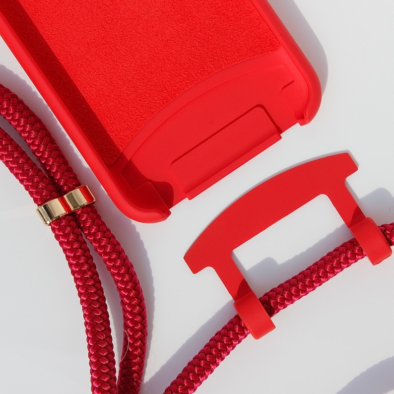 May include: A red phone case with a red and gold lanyard. The case has a textured surface and the lanyard has a gold accent.