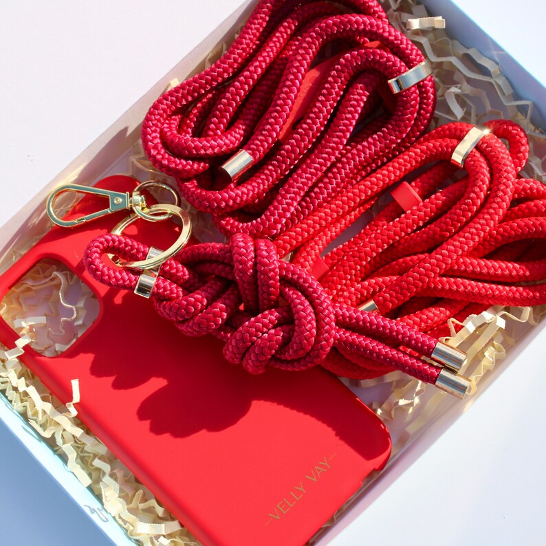 May include: A red phone case with a red rope phone strap and a gold key chain. The case has the text "Velly Vay" printed on the back.